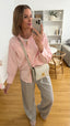 Frau trägt rosa Oversize-Bluse aus Baumwolle, kombiniert mit grauer Stoffhose und cremefarbener Crossbody-Tasche