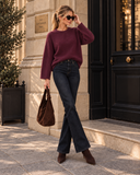 Frau in bordeauxrotem Pullover, dunkler Schlagjeans und Wildlederstiefeln mit brauner Tasche